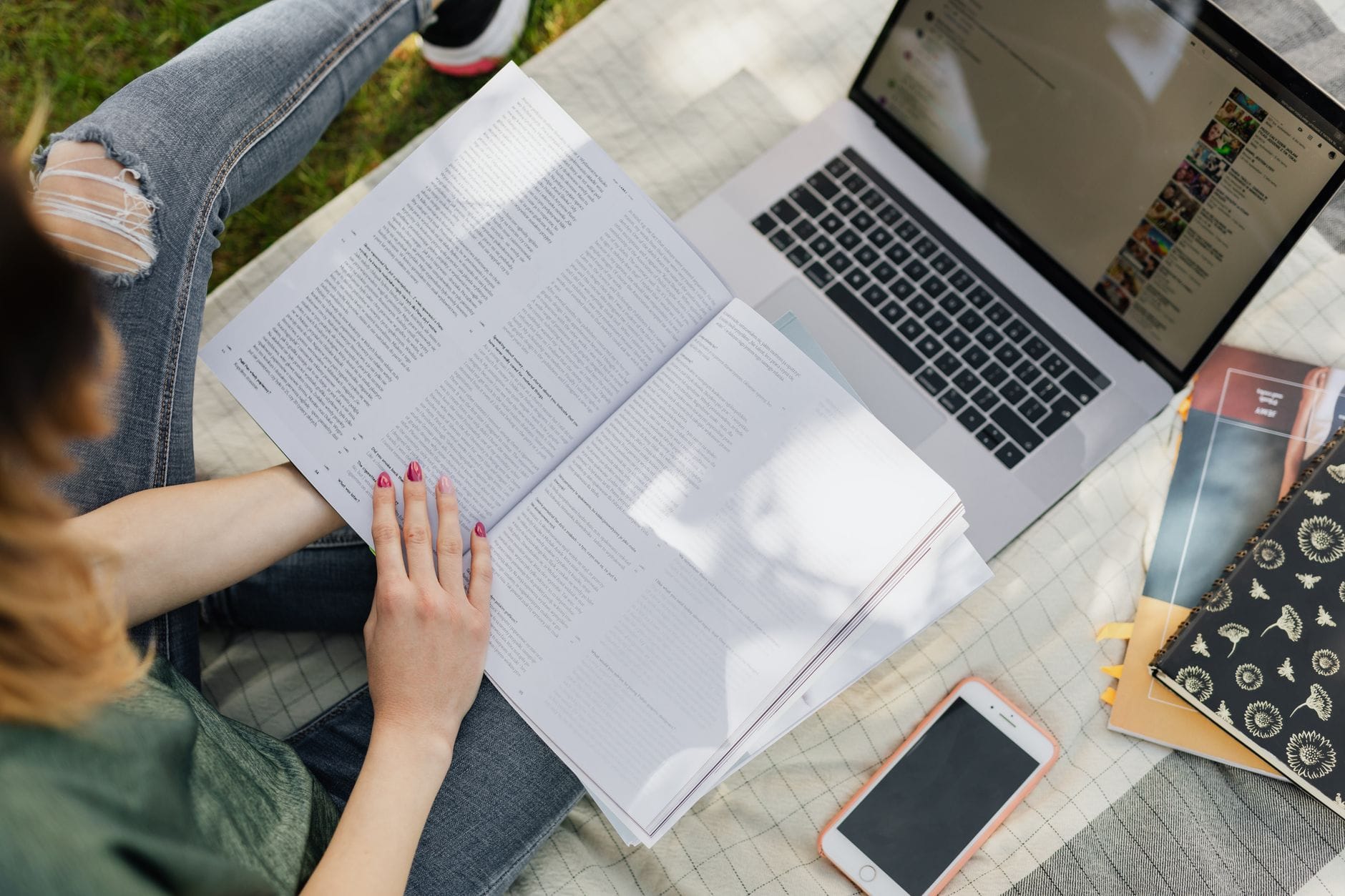 Studentka uczy się z podręcznika przy laptopie i telefonie w parku