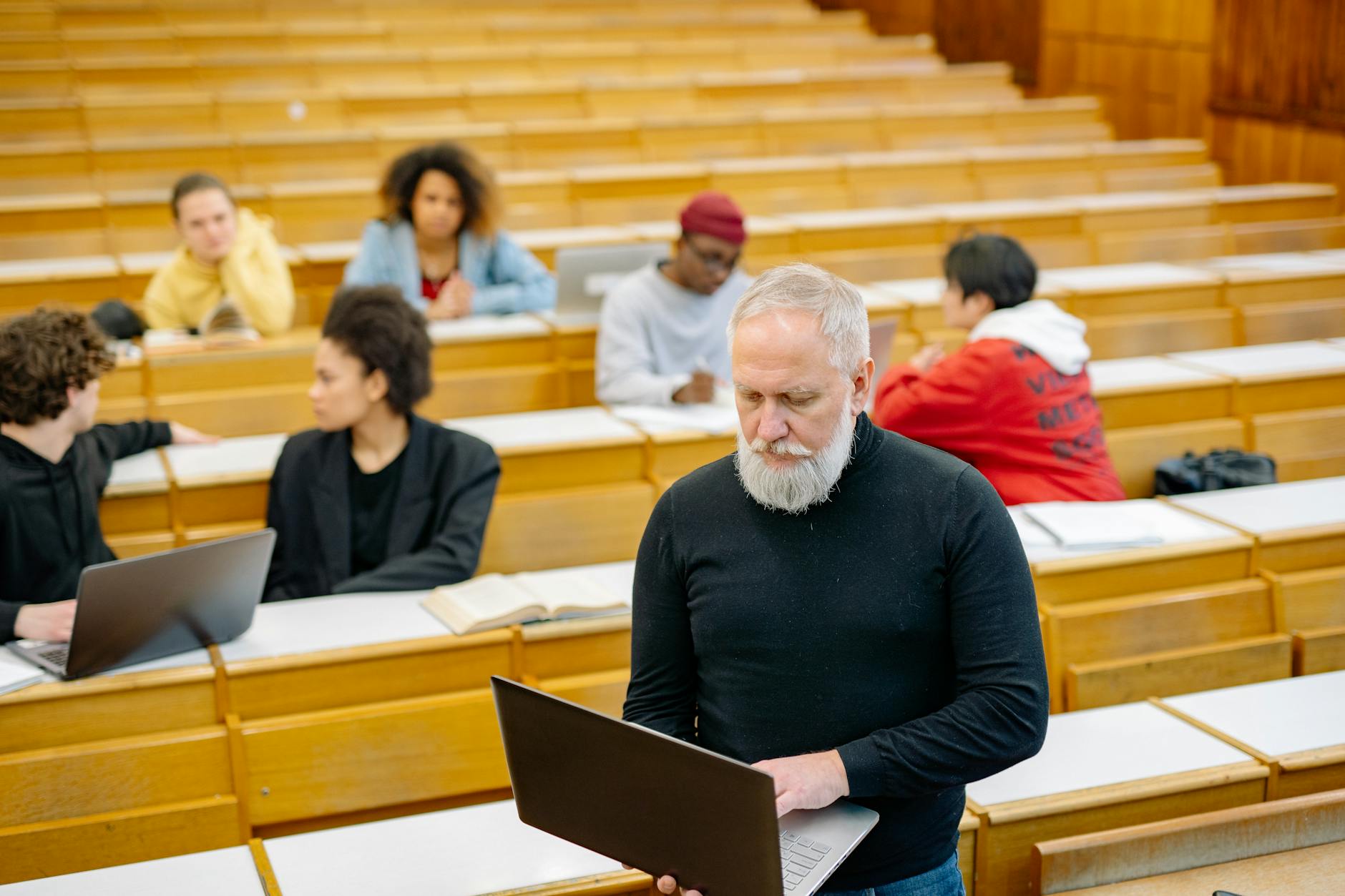 Wykładowca rozmawia ze studentami przy laptopach w dużej sali wykładowej
