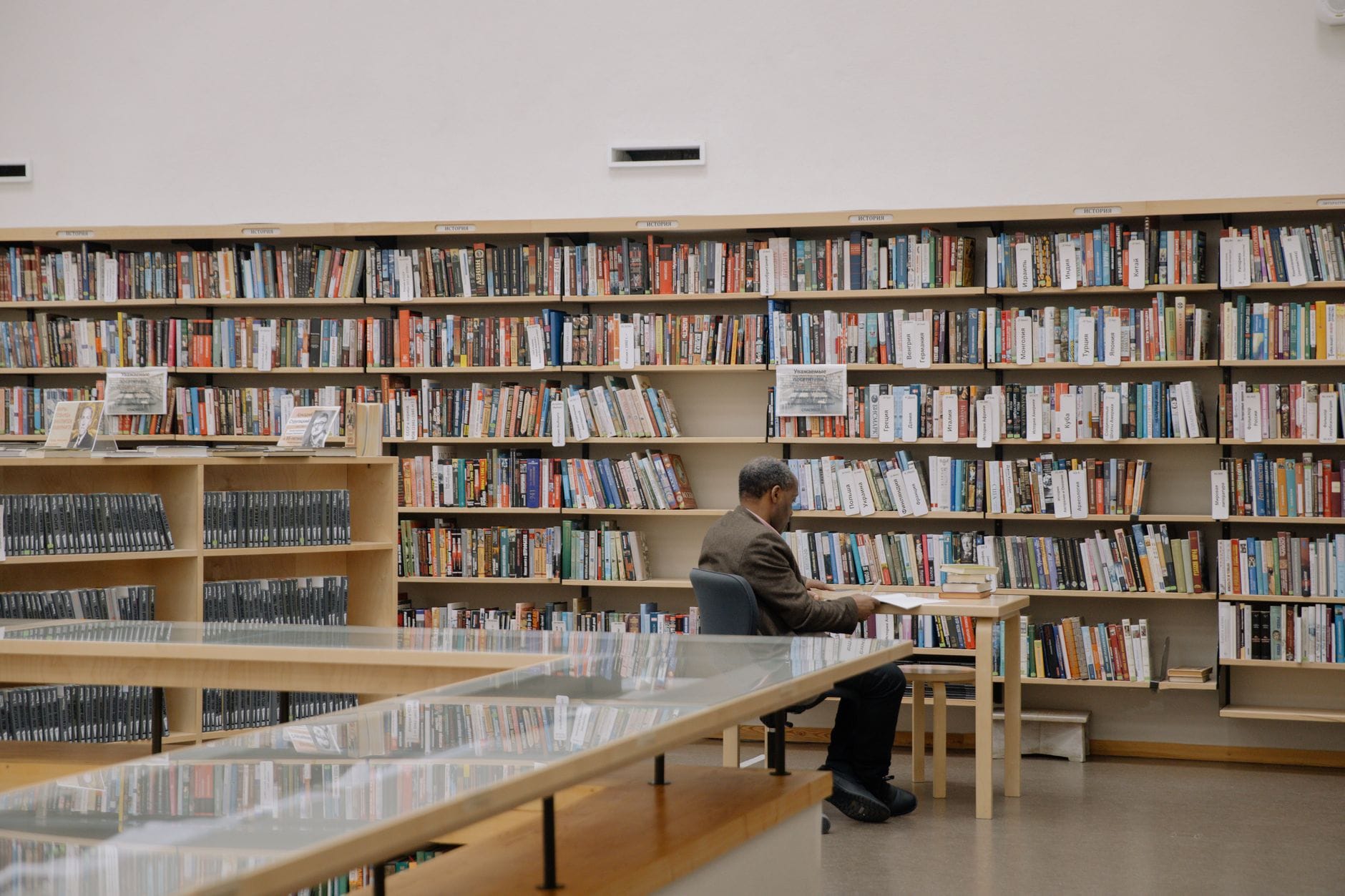 Mężczyzna czyta książkę przy stole w nowoczesnej, jasnej bibliotece
